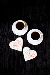 on a black background are two cups of coffee and biscuits in the form of heart