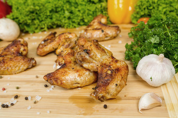 Fried chicken wings, baked chicken on a wooden board with cherry tomatoes, lettuce leaves, garlic, chilli pepper, rosemary, onion