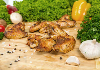 Fried chicken wings, baked chicken on a wooden board with cherry tomatoes, lettuce leaves, garlic, chilli pepper, rosemary, onion