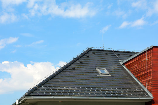 Shingles roof with skylights windows and rain gutter on the background of blue sky. Brick house with lightning conductor.