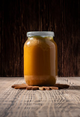 Glass jar with honey on a wooden tray on a wooden background.