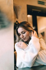 blonde girl in a cozy warm cafe, in a white knitted sweater 