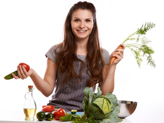 happy adult woman with various fresh vegetables on kitchen table looking at camera