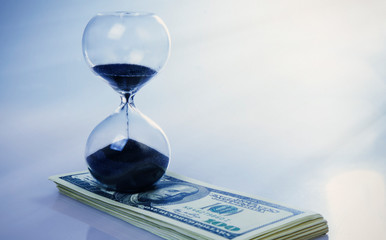 Concept: time is money. A sand clock and US Dollars as a symbol of work and opportunities in business.