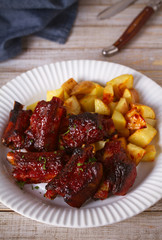 Grilled pork spare ribs with fries on white plate. Roasted sliced barbecue ribs. vertical