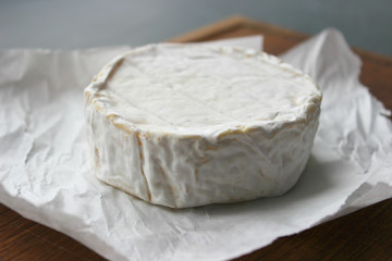 Camembert cheese close-up. Round Camembert cheese on the white paper, the background of the tree. Gourmet cheese, cheese plate, wine food. Camembert cheese. Fresh brie cheese and cut on a wooden Board