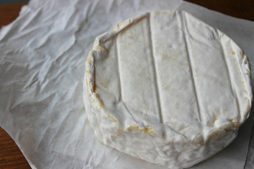 Camembert cheese close-up. Round Camembert cheese on the white paper, the background of the tree. Gourmet cheese, cheese plate, wine food. Camembert cheese. Fresh brie cheese and cut on a wooden Board