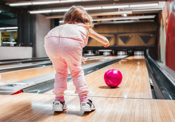 Young girl throwing a ball in bowling club. View from behind.