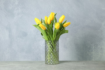 Beautiful yellow tulips in a glass vase on gray background for Mother's Day