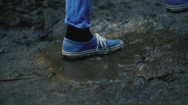 slow motion shot of a woman in blue jeans and dirty old blue vans innocently stepping into a dirty muddy puddle after a rain storm during winter 