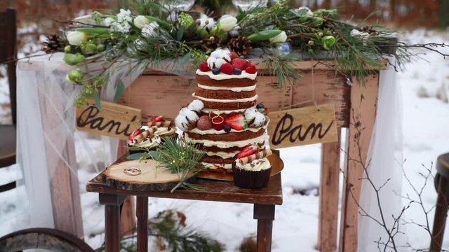 Winter wedding in the middle of a forest on a snow decoration old wooden table on it decorations of coniferous trees fruit cake candles of glasses inscription lady and lord with rings