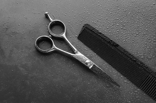 Hairdresser's scissors and comb with water drops, on gray background.