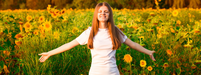 Young woman with long hair in sunflower Field with hands up. Beauty girl outdoors enjoying nature