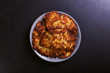 Hash brown and sour cream on a plate on a dark stone background, well fried. Copy space.