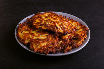 Hash brown and sour cream on a plate on a dark stone background, well fried. Copy space.