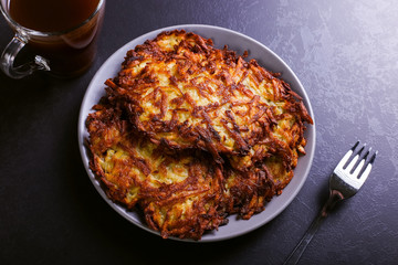 Hash brown and sour cream on a plate on a dark stone background, well fried. Copy space.
