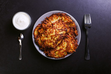 Hash brown and sour cream on a plate on a dark stone background, well fried. Copy space.