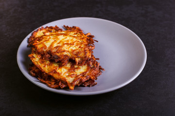 Hash brown and sour cream on a plate on a dark stone background, well fried. Copy space.