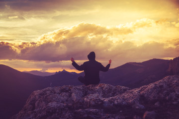 Young man meditates on the top of the mountain at sunset