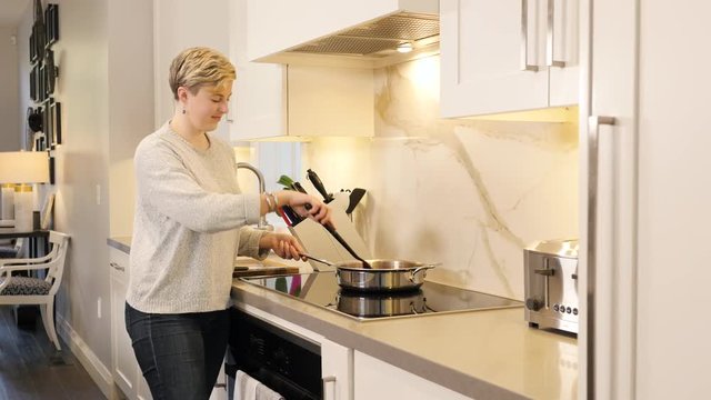 Slider shot of young woman cooking on stove in bright, clean kitchen