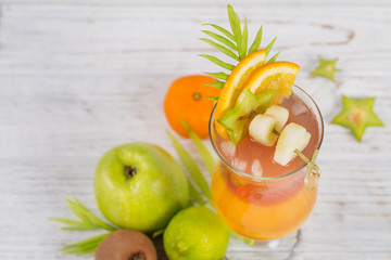 Summer cocktail with various tropical fruits around. Apple, kiwi, tangerine, orange, mango, carambola.