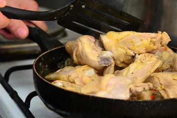The cook mixes fried chicken in a pan with butter and spices.