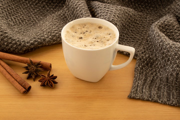 Cup of coffee with foam and scarf and cinnamon stick on wooden table