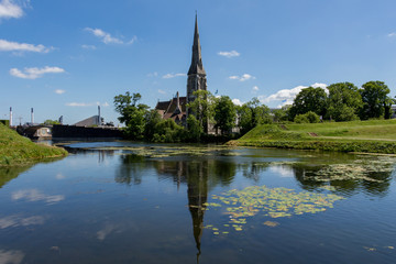 Fototapeta na wymiar St Alban's English Church located next to the citadel Kastellet in Copenhagen, Denmark. Small lake in from of the church. Reflection in the water. Bright, sunny day.