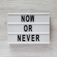 Top view, modern board with text 'Now or never' on a white wooden surface. Flat lay, overhead, from above.