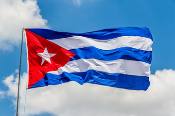 Cuban flag waving on the air. The flag is on a pole. It was designed in 1849 and officially adopted May 20, 1902. Blue sky with white clouds.