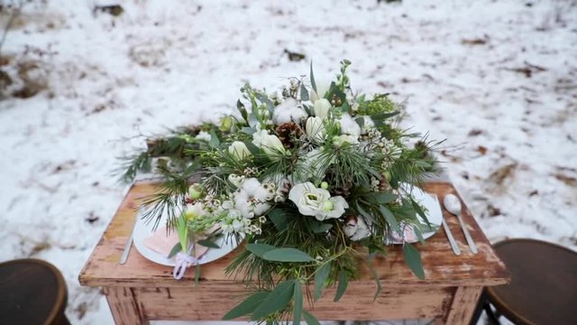 Winter wedding bouquet on table in the middle of forest on snow decoration old wooden table on it decoration of coniferous trees