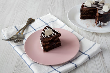 Piece of homemade chocolate cherry cake on a pink plate over white wooden background, side view.
