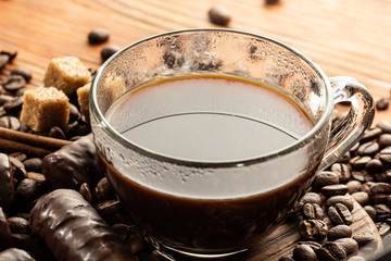 Close-up of coffee cup with roasted coffee beans on wooden background.