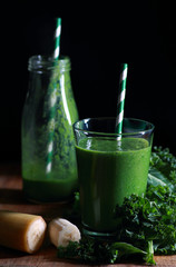 Green healthy kale smoothie in glass on dark background