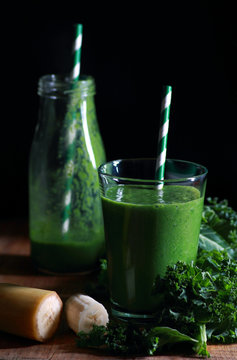 Green healthy kale smoothie in glass on dark background