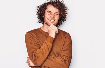 Fototapeta na wymiar Image of Caucasian male with curly hair smiling and posing for advertisement wears brown pullover, isolated on white wall with copy space for your promotion text. People, emotion and lifestyle concept