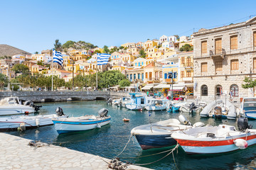 Fototapeta na wymiar Greek flags, boats and colorful neoclassical houses in harbor town of Symi (Symi Island, Greece)