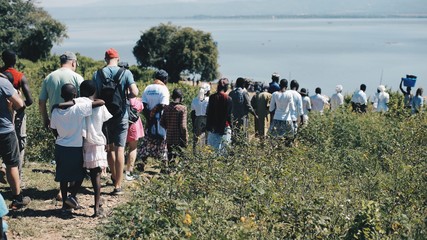 Big group of African and Caucasian people are going together to the shore of the sea.
