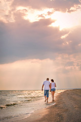 Fototapeta na wymiar couple in love walks along the sea holding hands surf at sunset, romantic honeymoon, summer