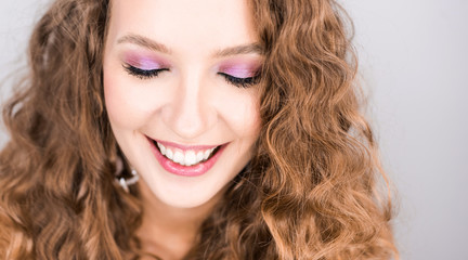 portrait beautiful young blonde curly girl posing in the studio with professional make-up and open  tooth smile pink mood