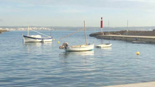 Traditional boats, llauts, moored in small bay near stone pier on a sunny day in Mallorca, Spain.