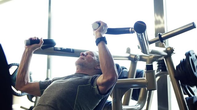 A senior man doing strength workout exercise in gym. Slow motion.