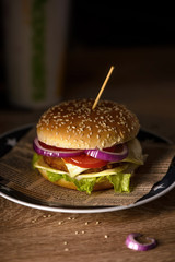 Hamburger with double cheese, red onions and tomatoes on a plate with white stars  on a table in the restaurant.