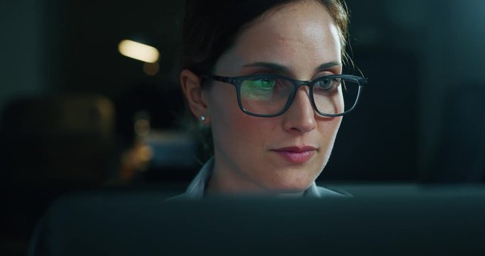 Slow motion of a young beautiful business woman wearing glasses working with a computer in a office. Shot in 8K. Concept of technology, business and finance, economy, management, success