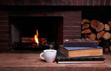 A cup of coffee and books on a wooden table in front of the fireplace