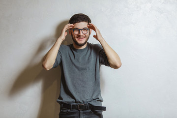 Portrait of young smiling man holding head with hands, over white textured background.