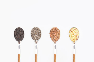 Different grains in spoons on white background. Chia, flax, black sesame seeds and grain mix. Flat lay. Top view