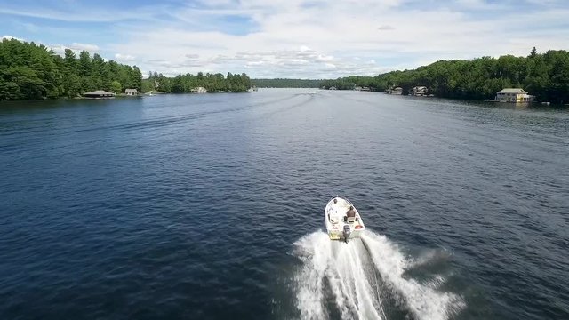 Aerial footage of a white motor boat travelling down a narrow lake.