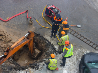 A group of road workers from public utilities in reflective special vests are discussing an emergency when digging a hole to eliminate the leakage of pipes in the middle of winter
