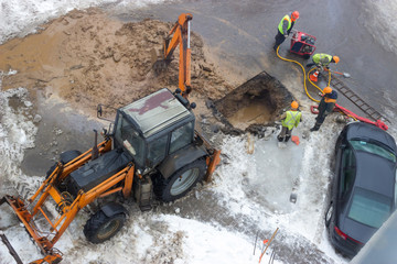 A group of road workers from public utilities in reflective special vests are discussing an emergency when digging a hole to eliminate the leakage of pipes in the middle of winter